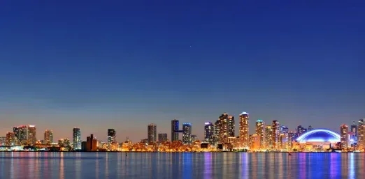 The Toronto skyline across the lake at dusk, with the lit dome of the Rogers Centre